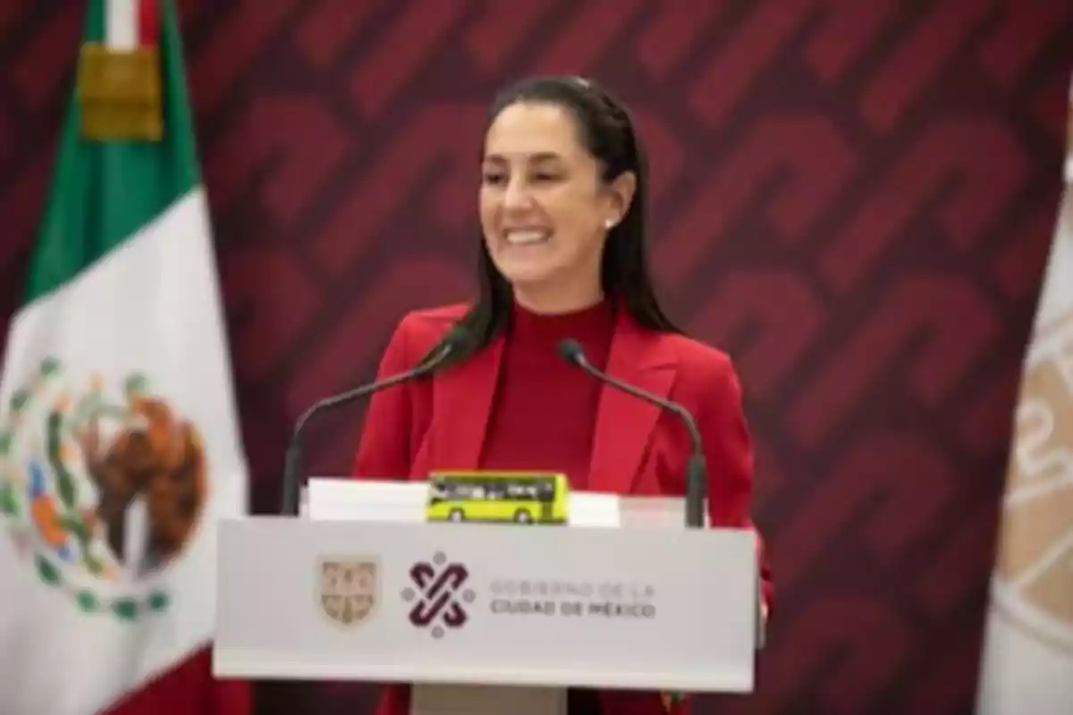 Una persona hablando en un podio con el logotipo del Gobierno de la Ciudad de México, con una bandera de México al fondo.