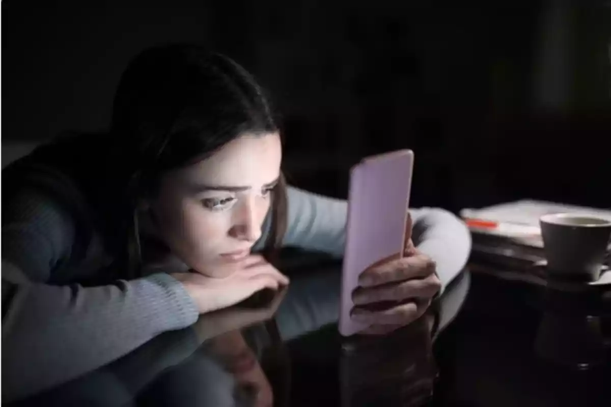 Mujer mirando su teléfono móvil con expresión seria en un ambiente oscuro.