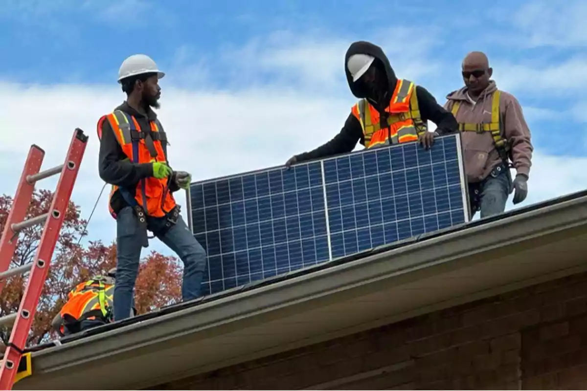 Tres trabajadores con equipo de seguridad instalan un panel solar en el techo de un edificio.