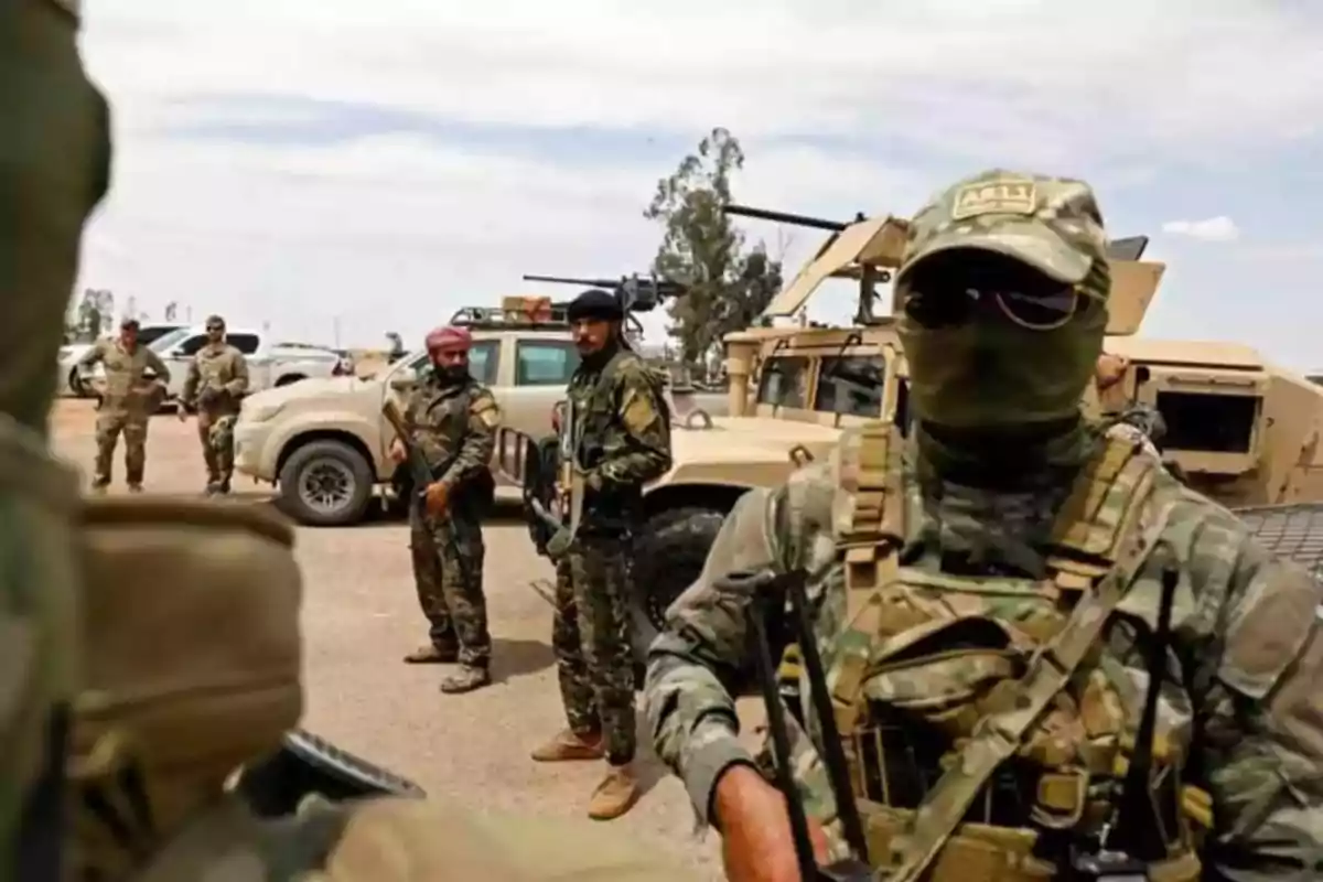 Soldados armados con equipo militar y vehículos en un entorno al aire libre.