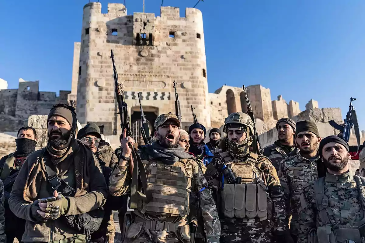 Grupo de hombres armados con uniformes militares frente a una antigua fortaleza de piedra.