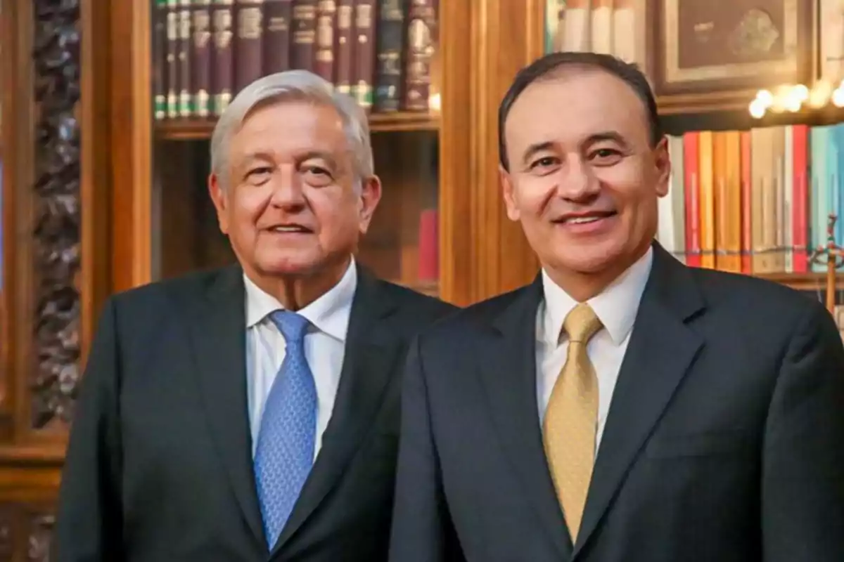 Two men in suits pose together in front of a bookshelf.