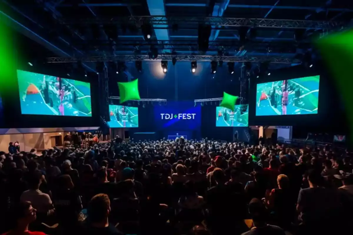 Una multitud asiste a un evento en un auditorio con pantallas grandes y luces verdes.