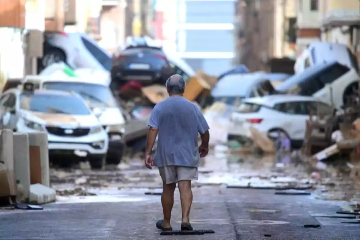 Un hombre camina por una calle llena de escombros y autos dañados tras un desastre natural.