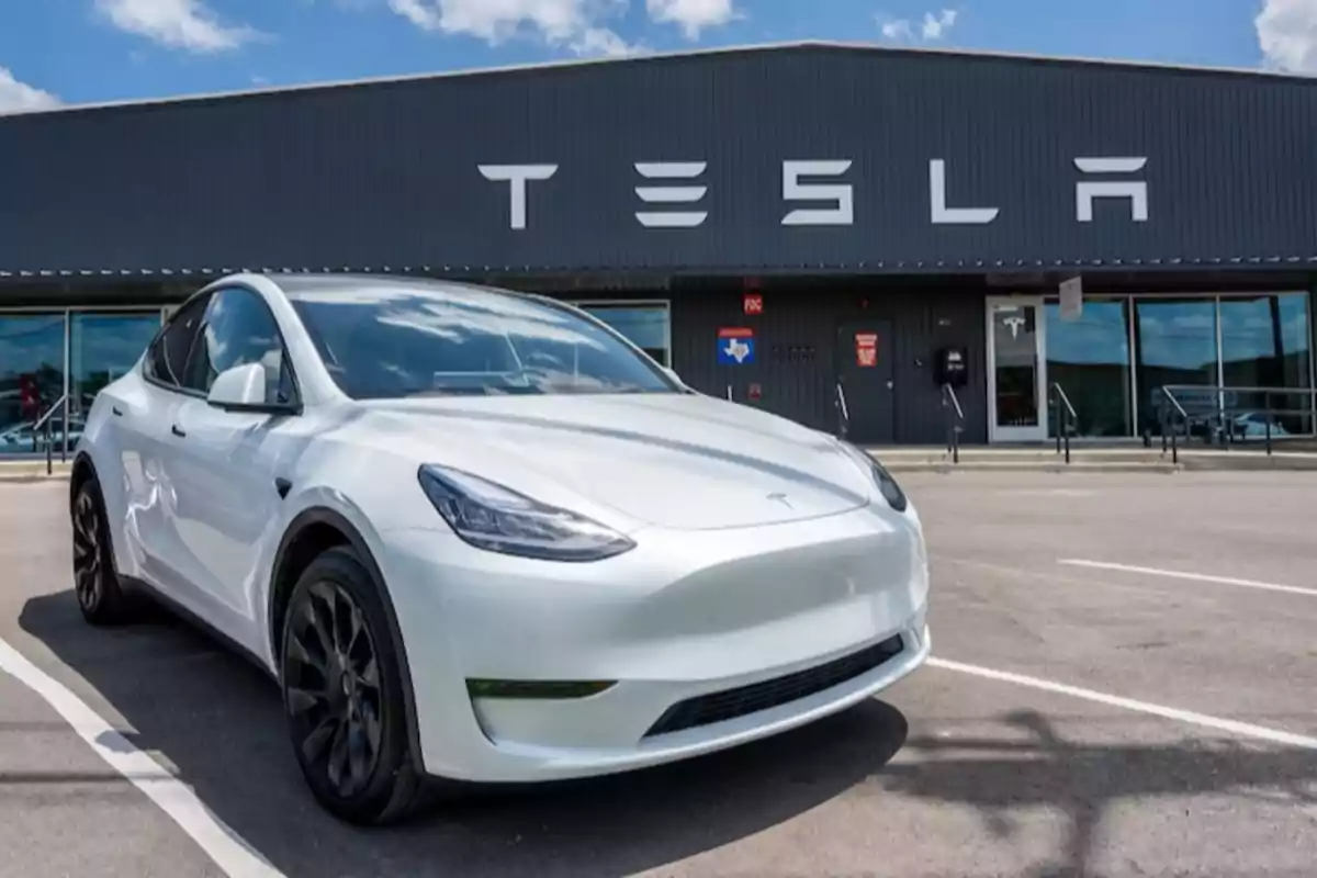 A white electric car parked in front of a building with the Tesla logo.