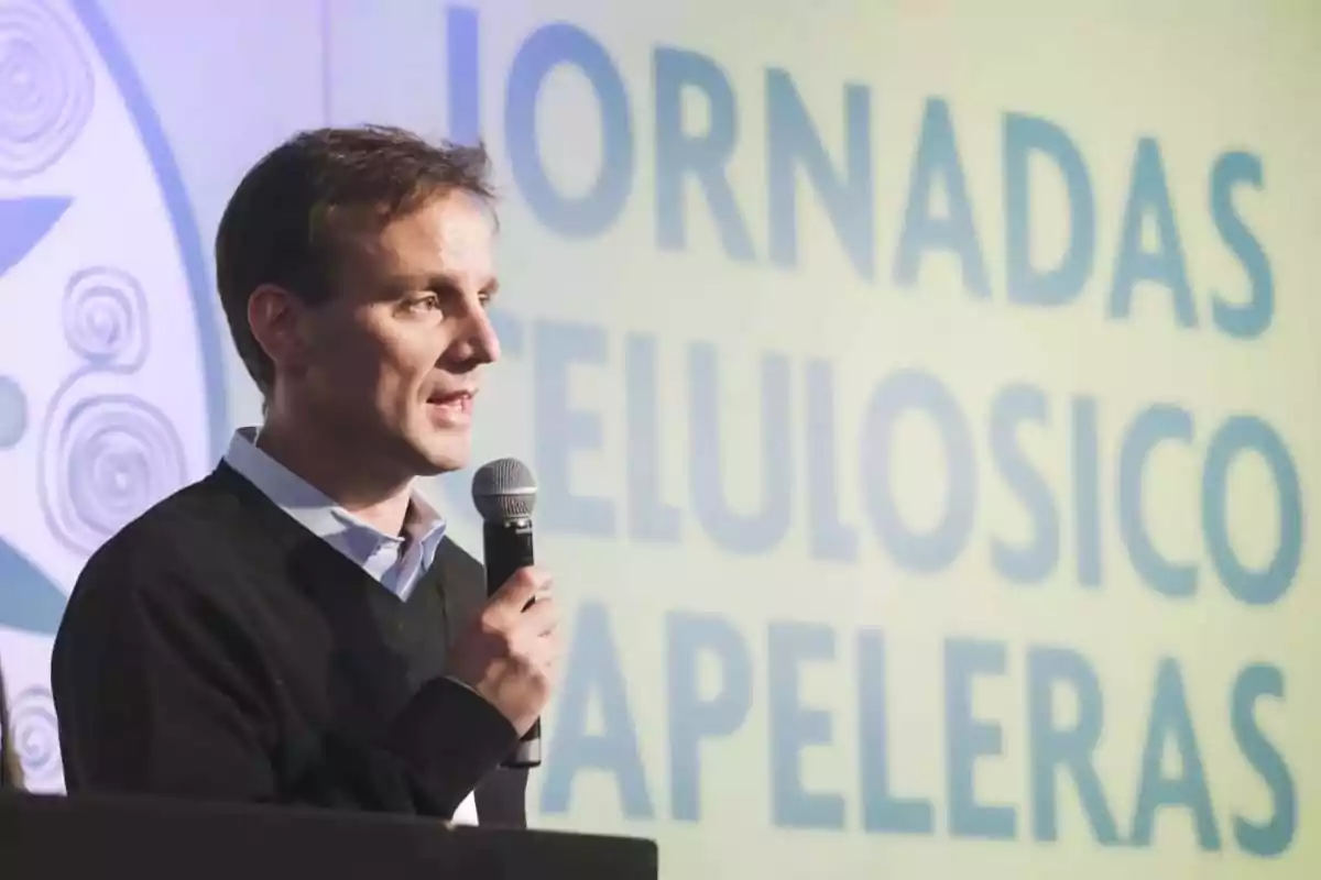 Hombre hablando en una conferencia con un micrófono en la mano y un cartel de fondo que dice "Jornadas Celulósico Papeleras".