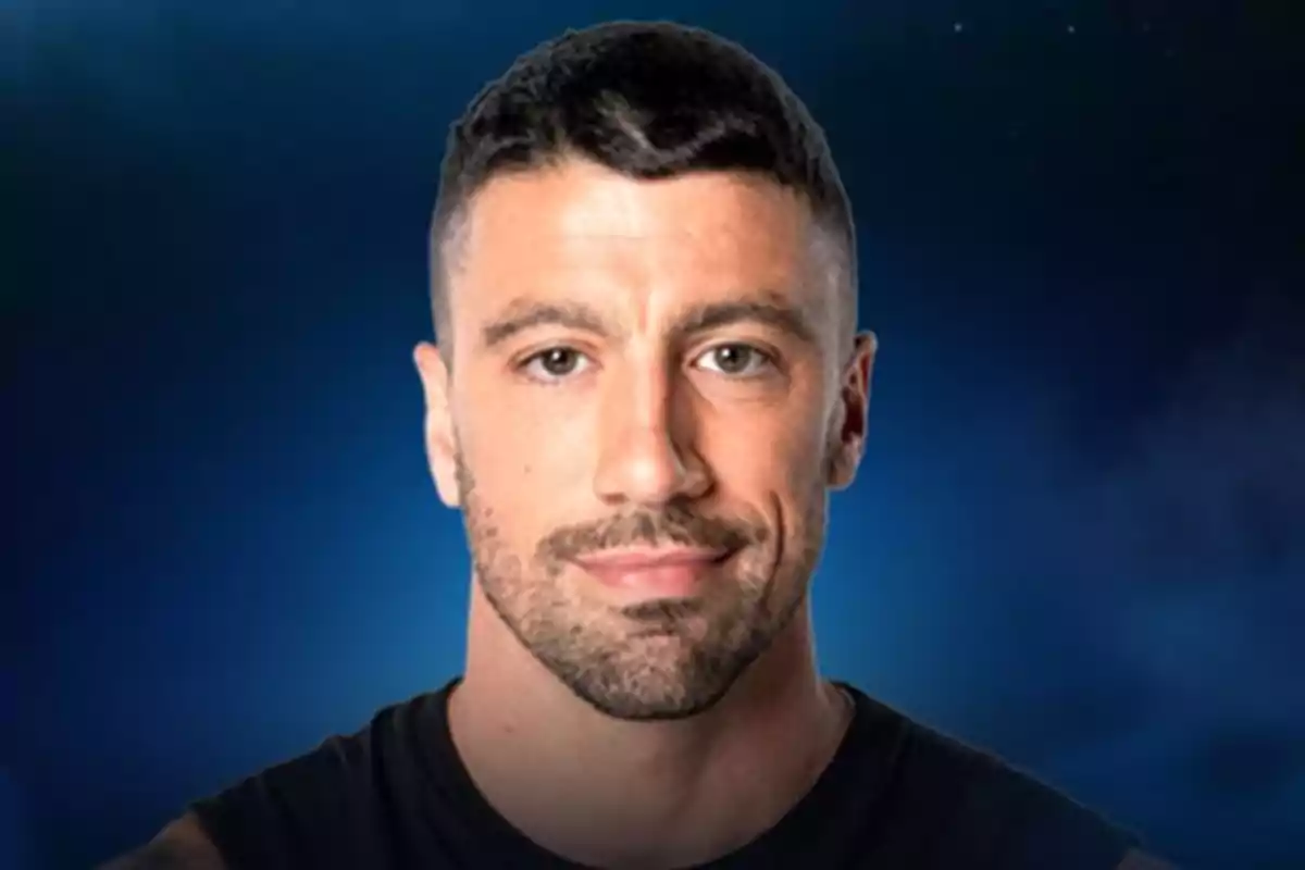 Un hombre con cabello corto y barba ligera sobre un fondo azul oscuro.