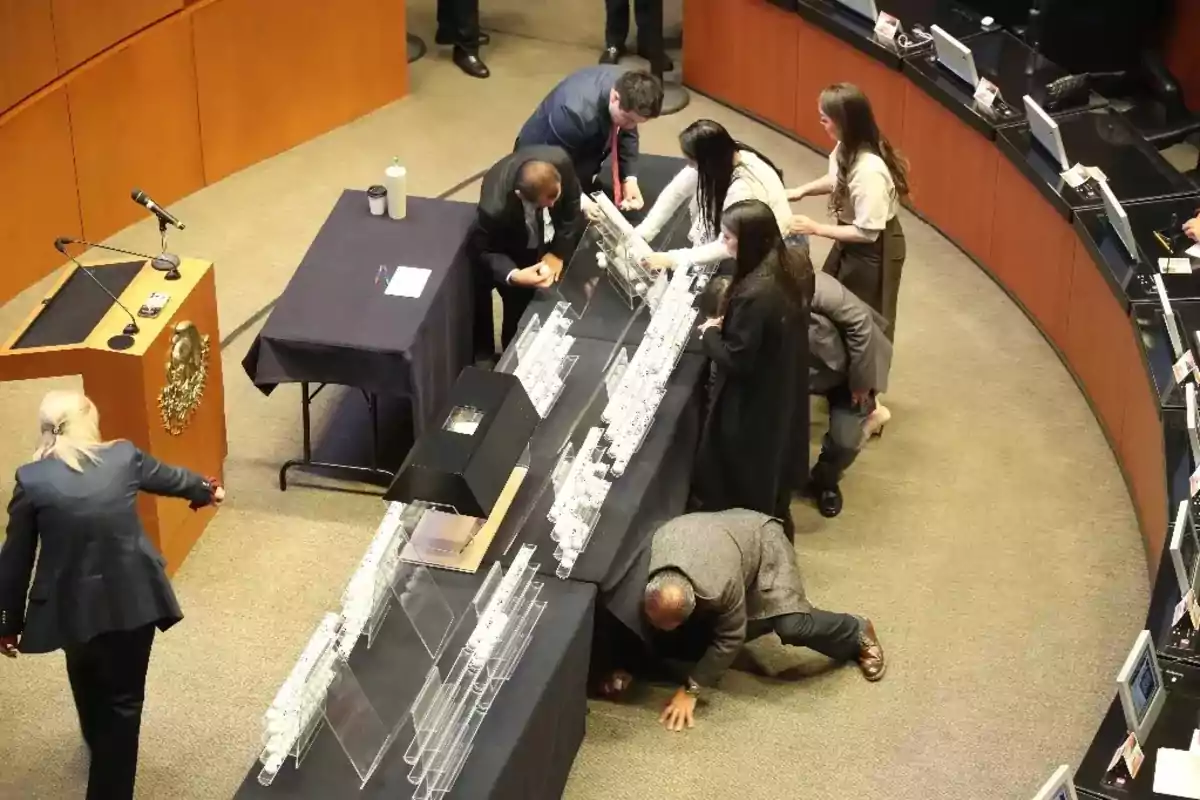 Personas reunidas alrededor de una mesa en un entorno formal, observando y manipulando objetos transparentes.