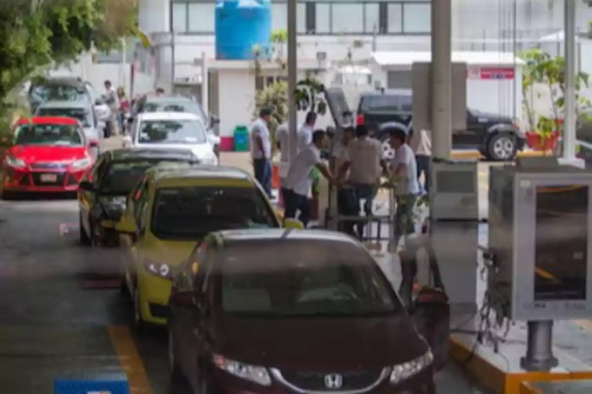 A line of cars at a vehicle inspection center with several people around an inspection machine.