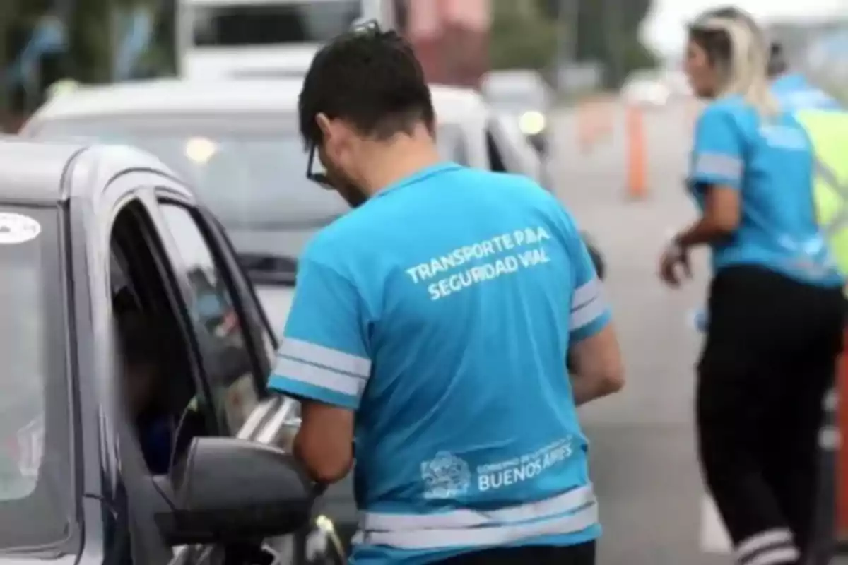 Un agente de tránsito con una camiseta azul interactúa con un conductor en un control vehicular en la vía pública.