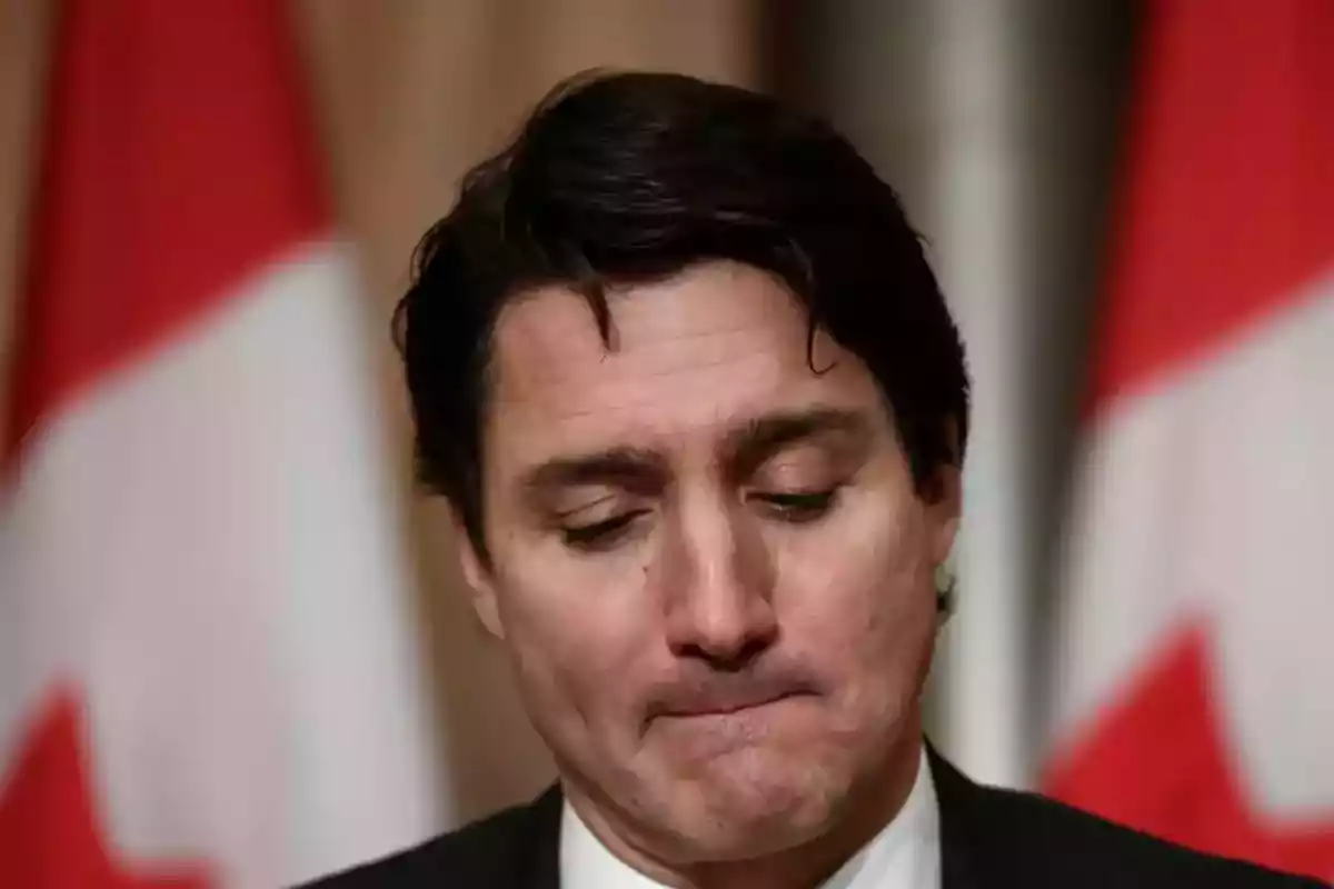 Un hombre con expresión seria y banderas de Canadá de fondo.