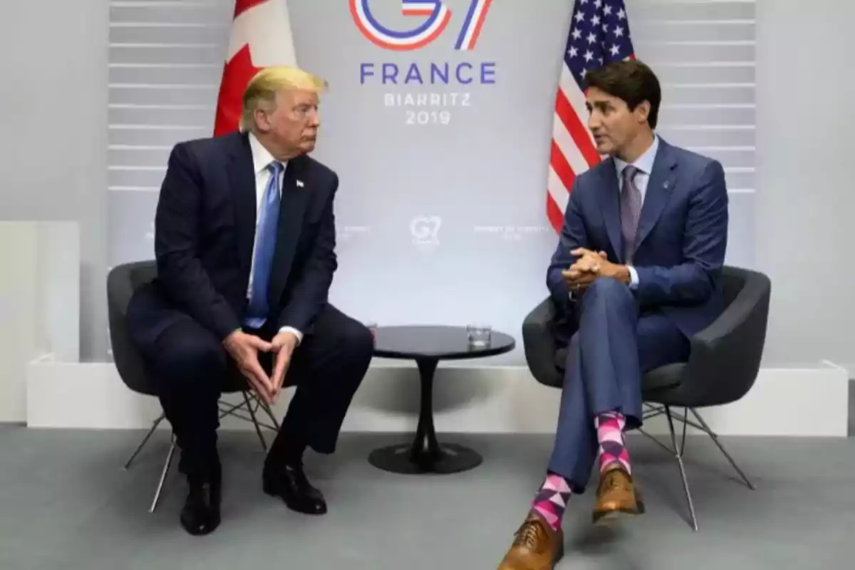 Dos personas sentadas en sillas frente a frente en una reunión del G7 en Biarritz 2019 con banderas de Canadá y Estados Unidos de fondo.