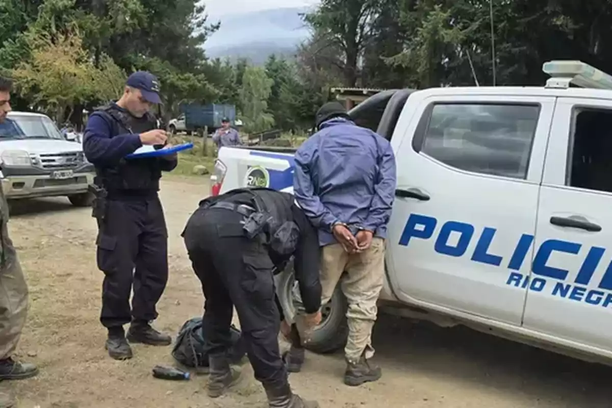 Un grupo de policías realiza un arresto junto a una camioneta en un entorno rural.