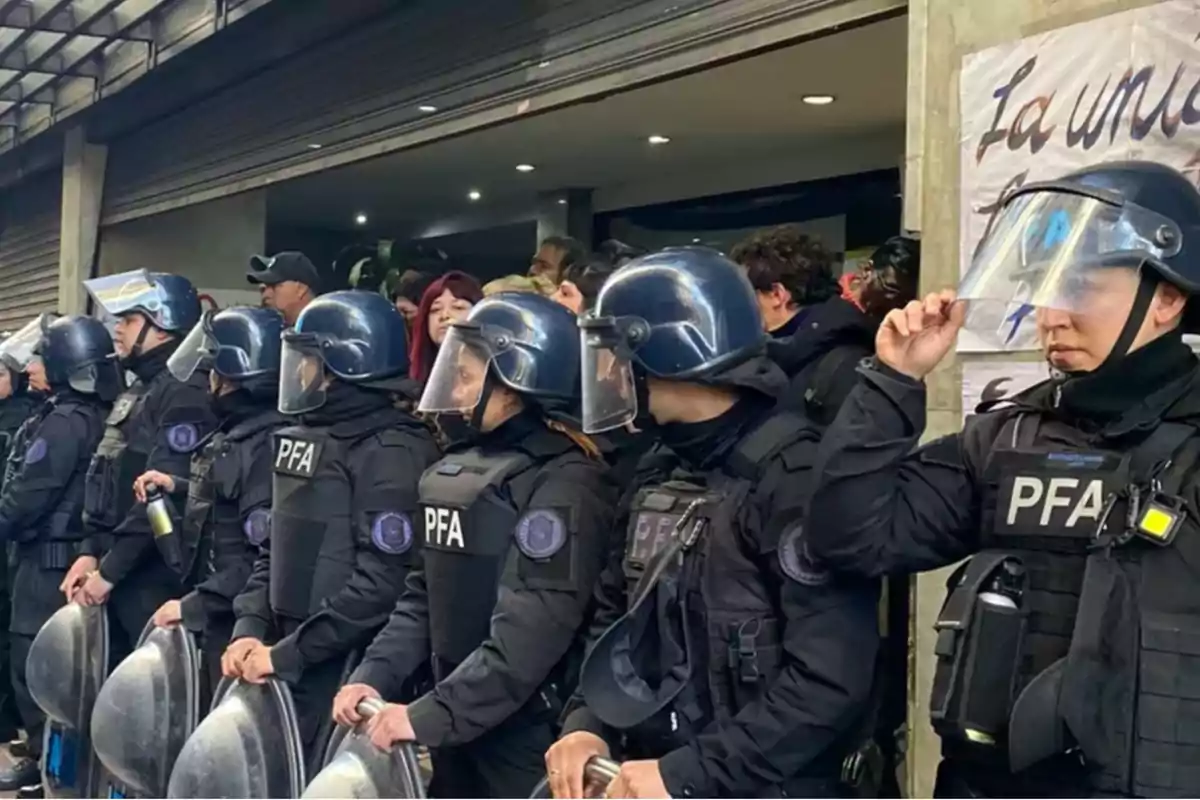 Policías con equipo antidisturbios de la PFA en formación frente a una multitud.