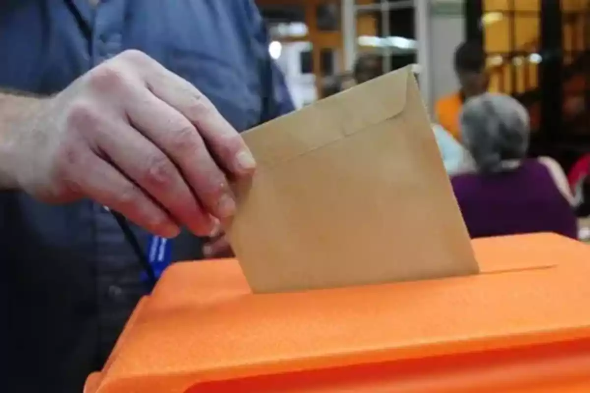 Persona depositando un sobre en una urna de votación.