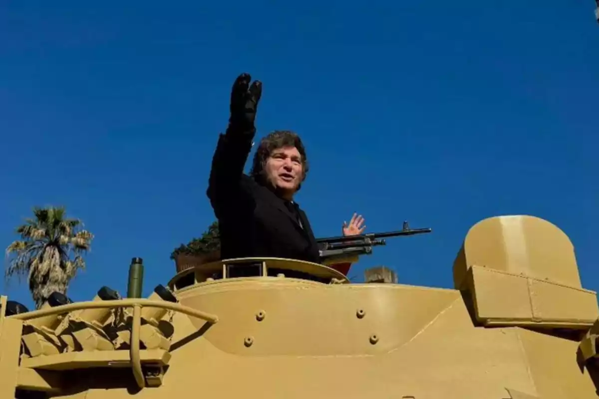 Una persona saludando desde un vehículo militar bajo un cielo despejado.