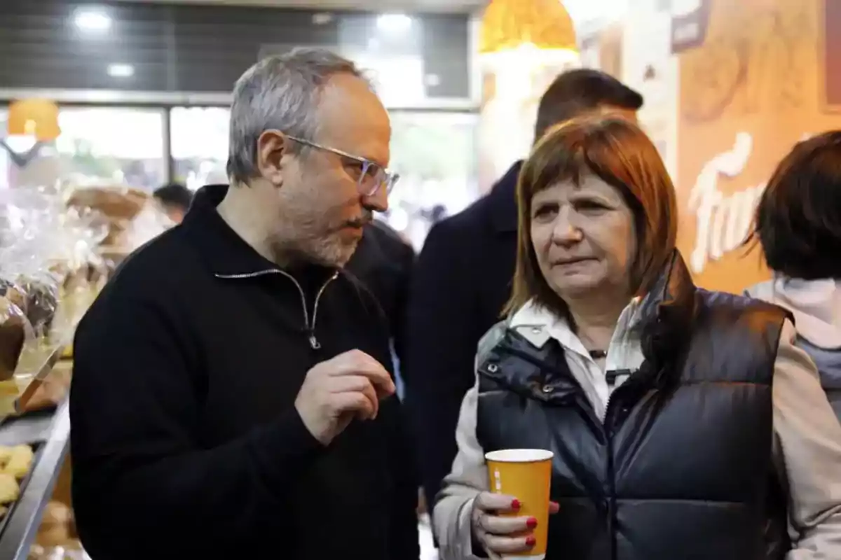 Dos personas conversando en una panadería mientras una de ellas sostiene un vaso de papel.