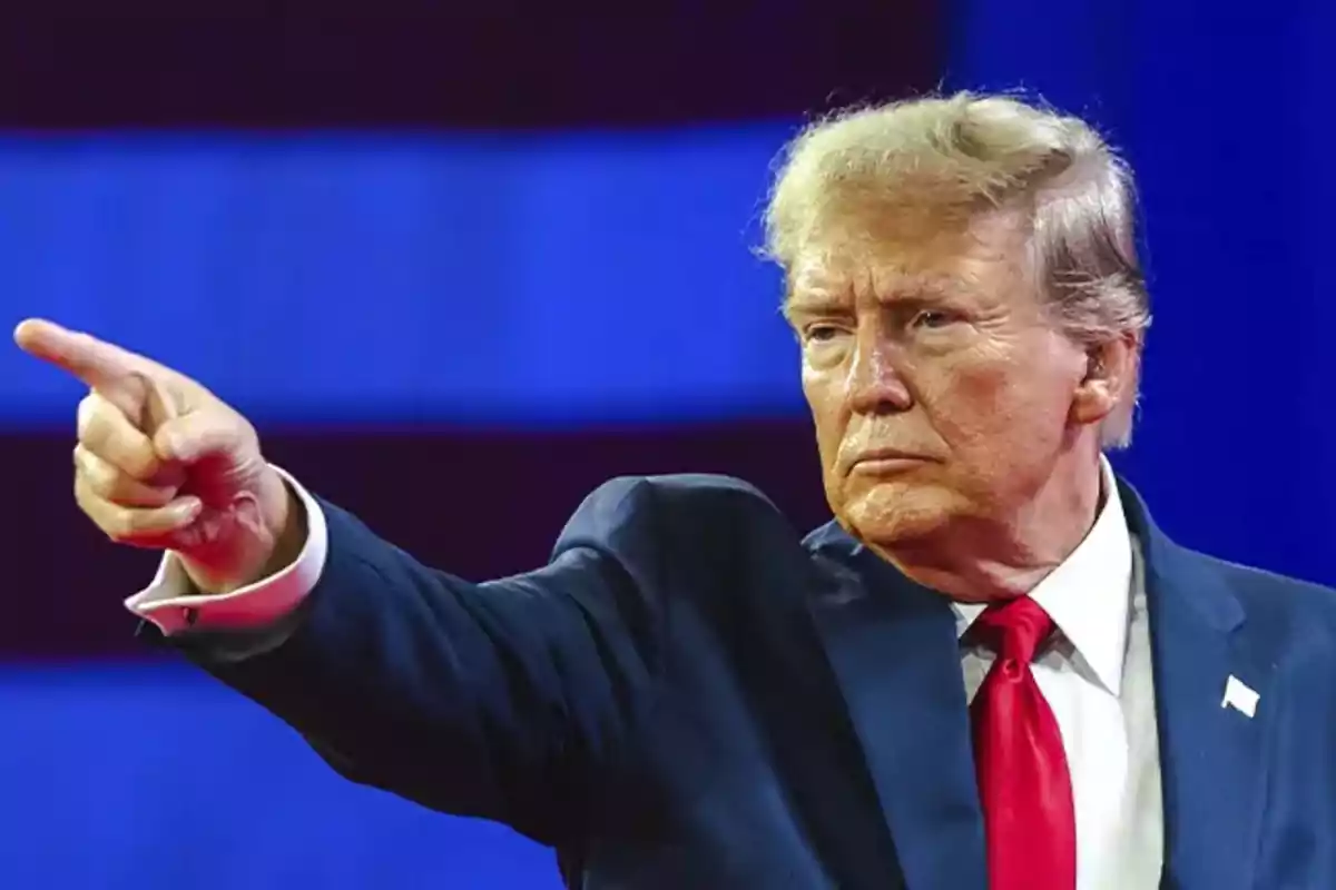 A man in a blue suit and red tie points with his finger against a blue background.