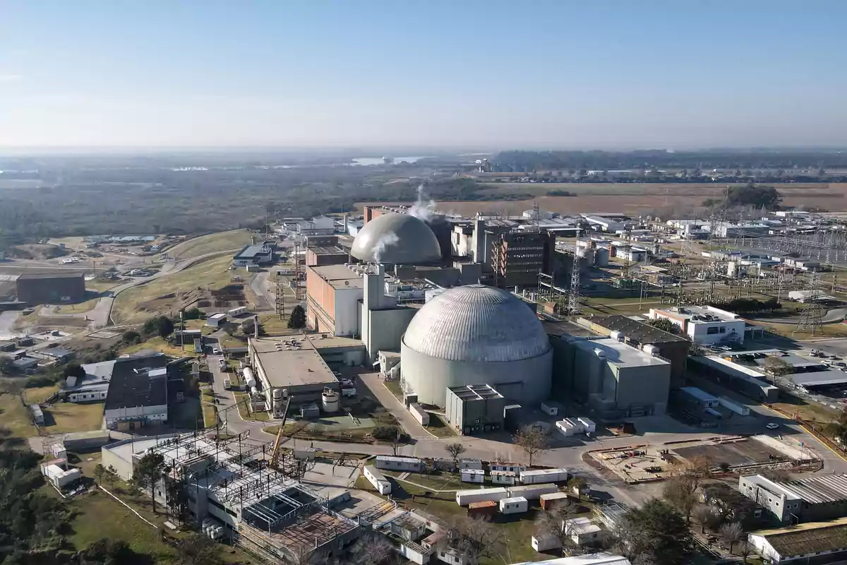 Vista aérea de una planta nuclear con dos grandes cúpulas y varias edificaciones industriales rodeadas de áreas verdes y caminos.