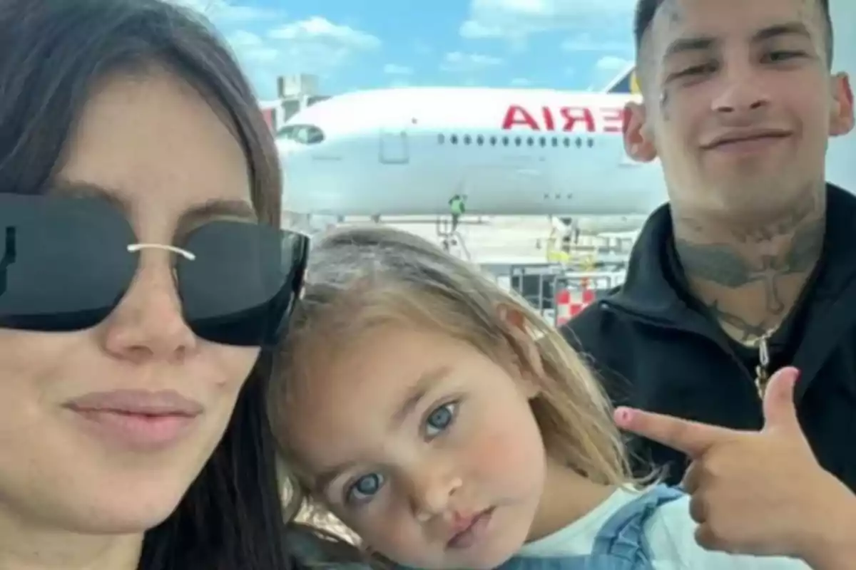 Una familia sonriente posando frente a un avión en un aeropuerto.