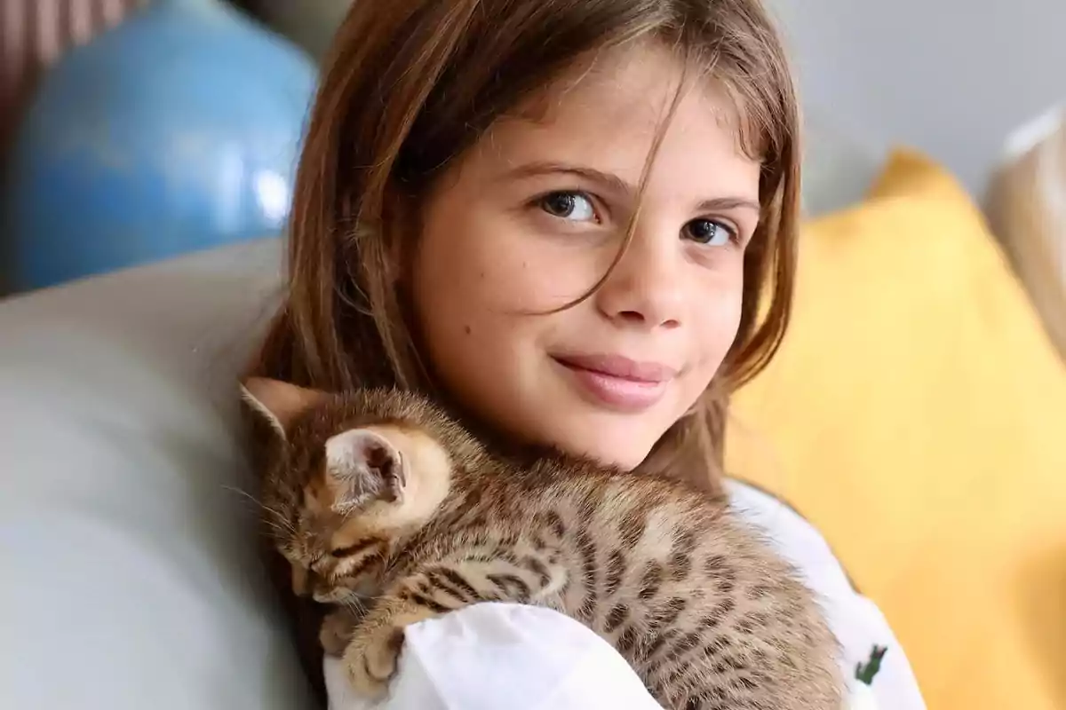 Una niña sonriente sostiene un gatito dormido en sus brazos.