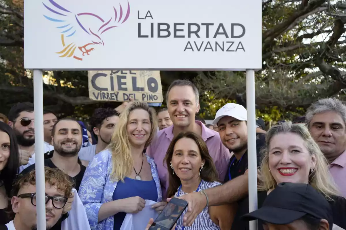 Un grupo de personas sonríe frente a un cartel que dice "La Libertad Avanza" con un logo de un ave.