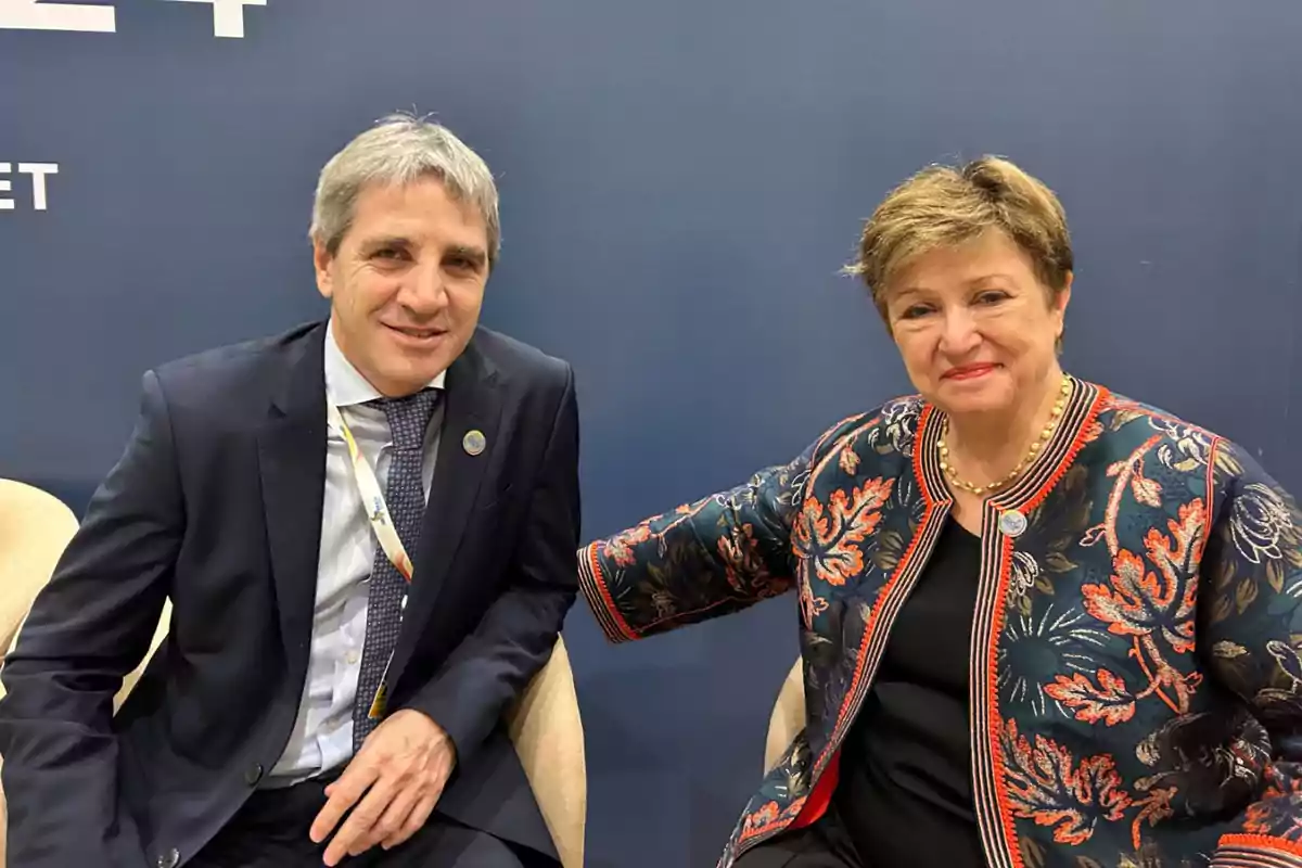 Dos personas sentadas juntas sonriendo frente a una pared azul.