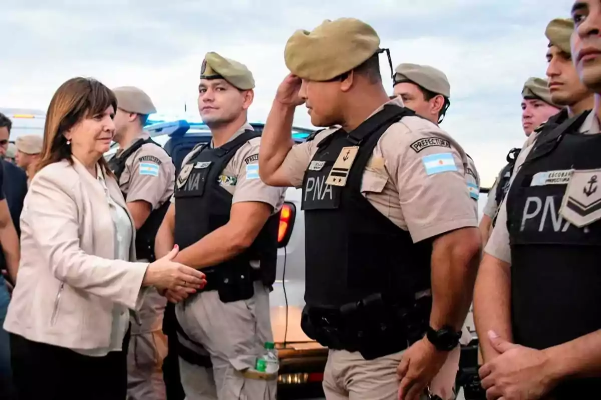 Una mujer estrecha la mano de un oficial de la Prefectura Naval Argentina mientras otros oficiales observan.