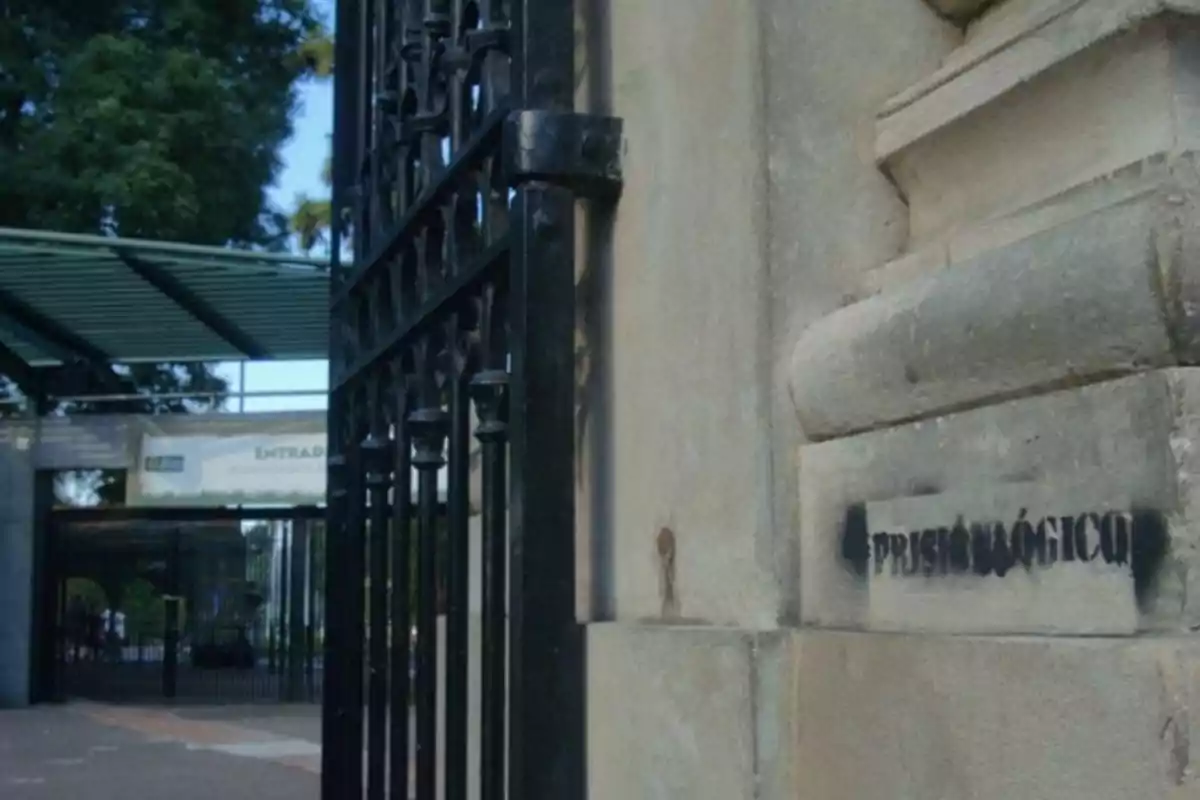 Entrada principal de un zoológico con una puerta de hierro forjado y un letrero que dice "PRESIDIO LÓGICO" en la pared.