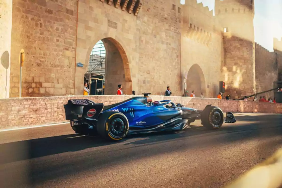 Un coche de carreras azul pasando frente a una antigua muralla de piedra.