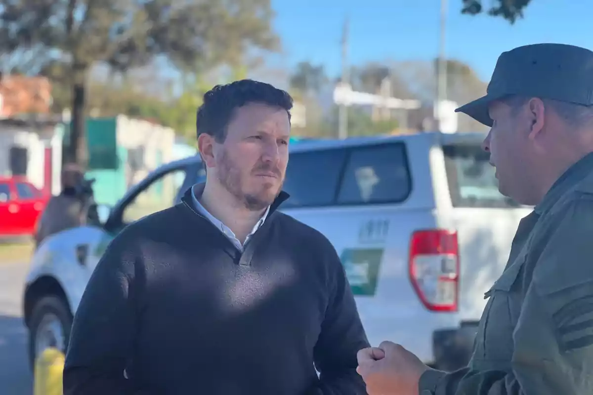 Dos hombres conversando al aire libre con una camioneta de fondo.