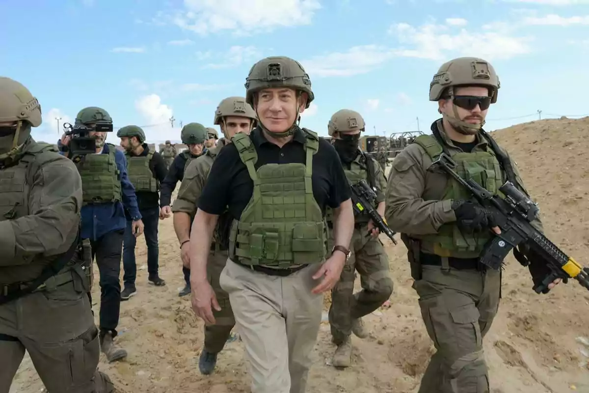 Un grupo de personas con equipo militar camina por un terreno arenoso bajo un cielo parcialmente nublado.