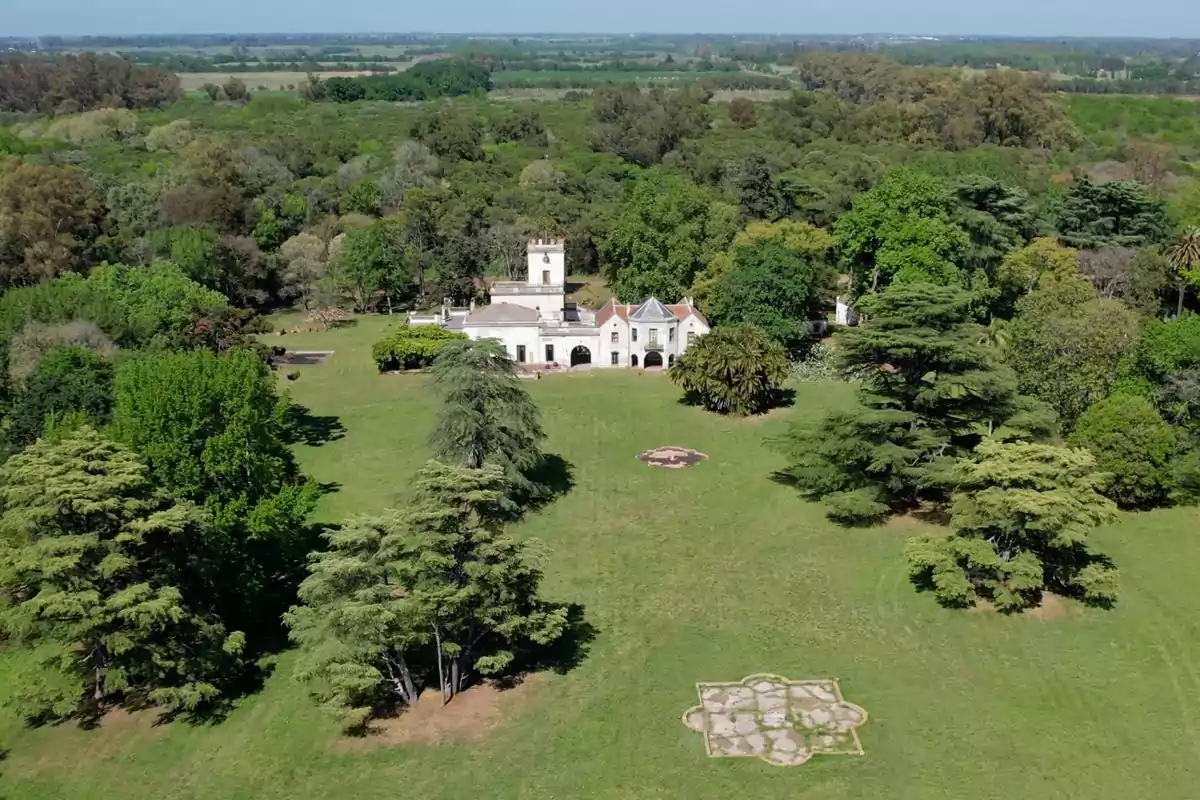 Vista aérea de una casa grande rodeada de un extenso jardín verde y árboles frondosos.