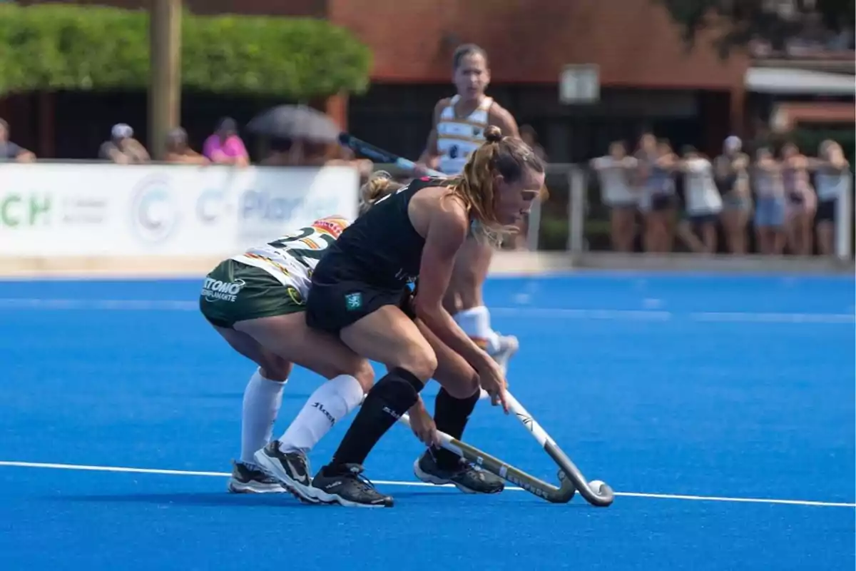 Jugadoras de hockey compiten intensamente en un campo azul durante un partido.