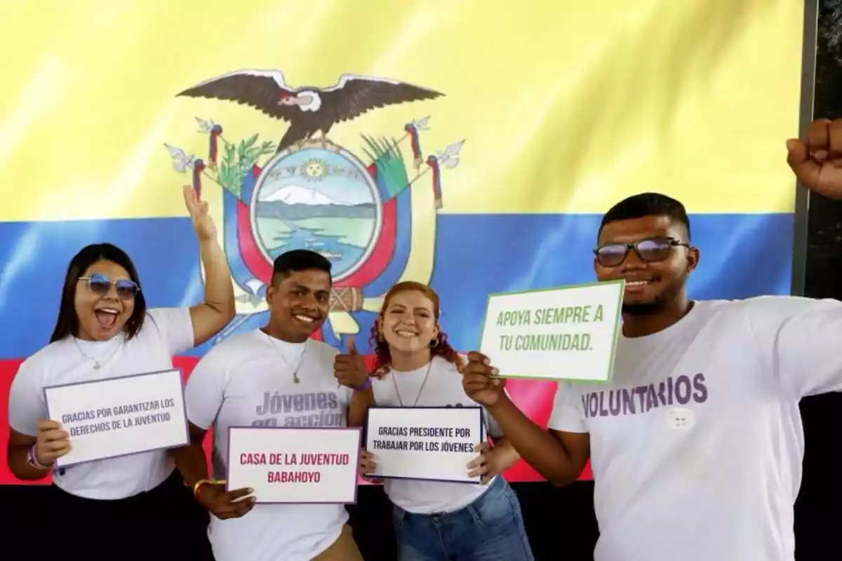 A group of smiling young people hold signs with positive messages in front of an Ecuadorian flag.