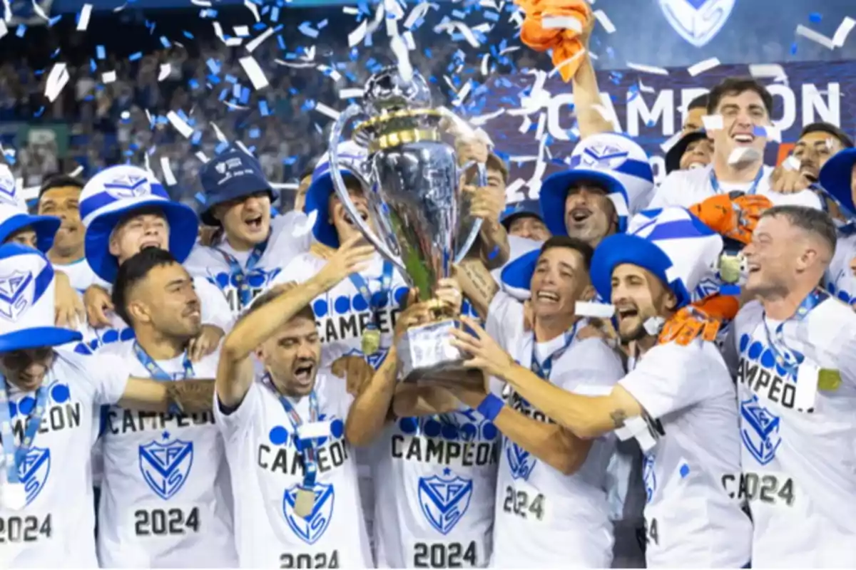 Un equipo de fútbol celebra con entusiasmo mientras levanta un trofeo, rodeados de confeti azul y blanco.