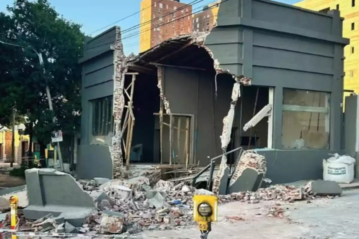 Edificio con fachada parcialmente colapsada y escombros en la acera.