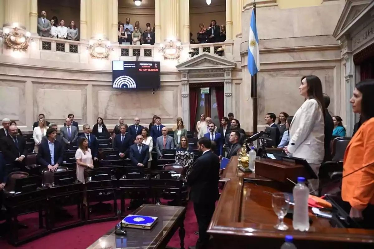 Personas reunidas en un recinto parlamentario con una pantalla que indica "No hay quórum" y una bandera argentina visible.