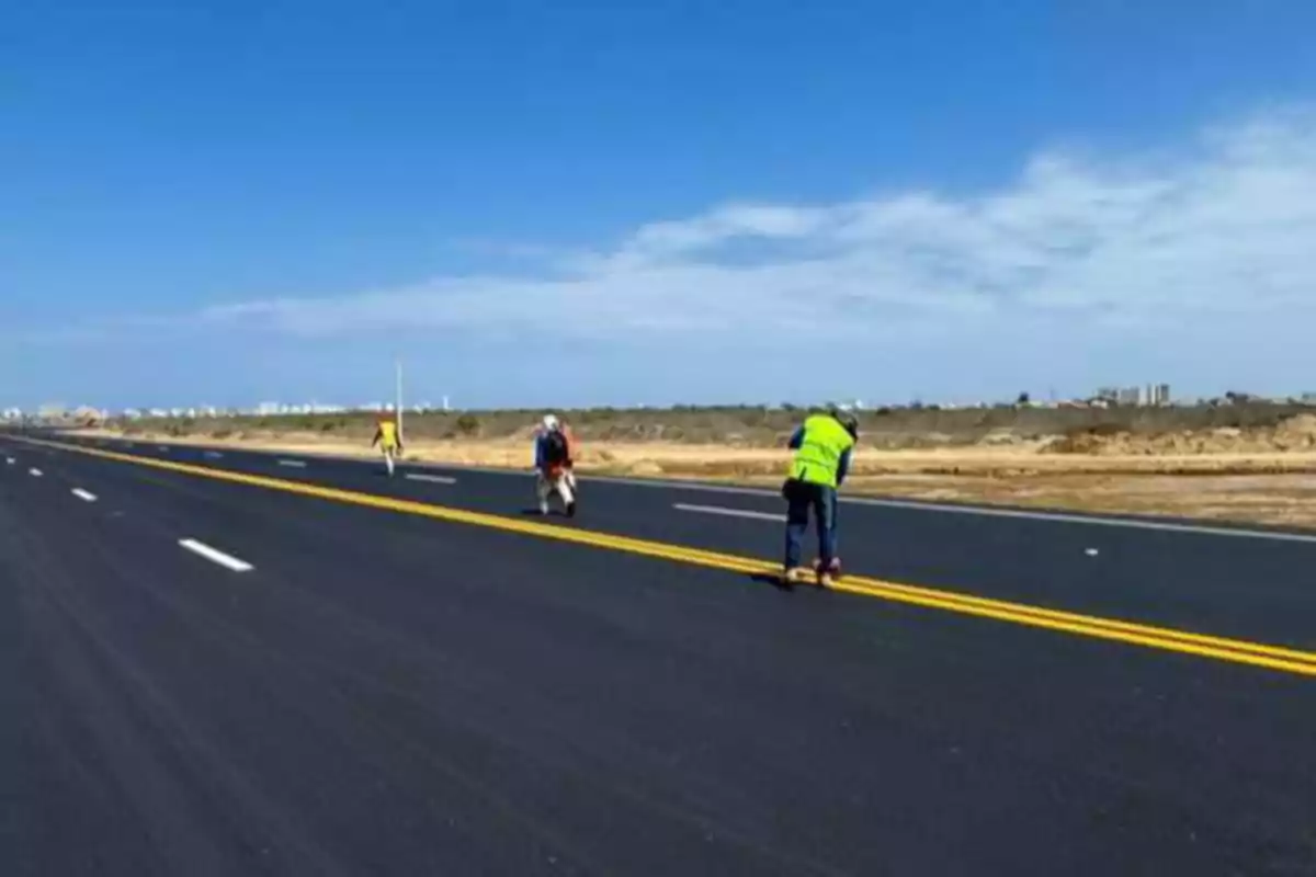 Trabajadores pintando líneas amarillas en una carretera recién asfaltada bajo un cielo despejado.