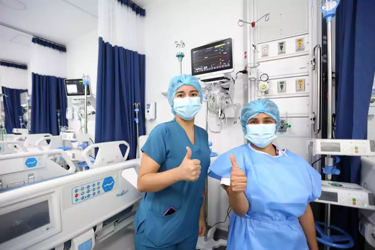 Personal médico con equipo de protección en una sala de hospital dando un gesto de aprobación.