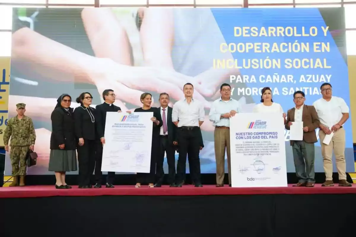 Un grupo de personas en un escenario sosteniendo carteles grandes durante un evento de desarrollo y cooperación en inclusión social en Ecuador.