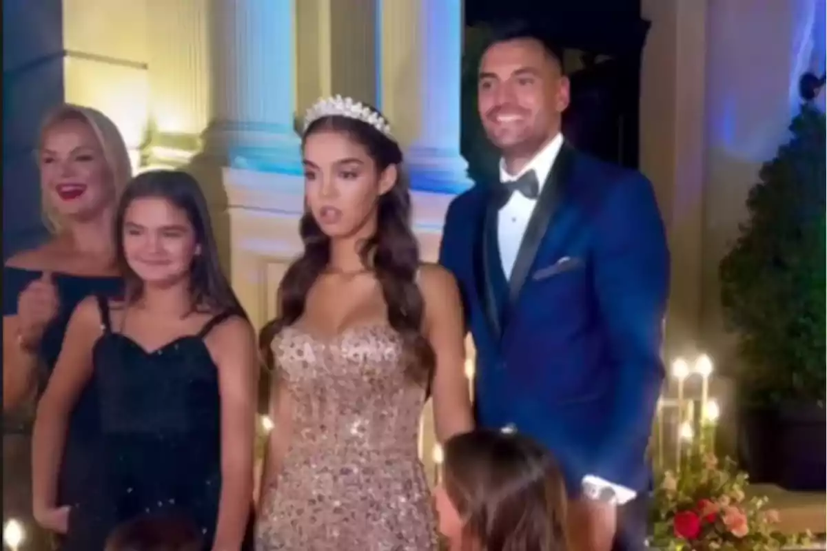 Un grupo de personas posando para una foto en un evento elegante, con una joven en el centro usando un vestido brillante y una tiara.