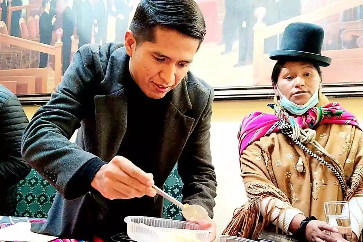 A man serving food in a container while a woman in traditional attire watches.